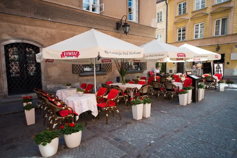 Duże, kwadratowe parasole restauracyjne w kolorze białym z logo Żywiec, osłaniające ogródek letni
